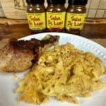 Plate with chicken leg and mac and cheese with 3 salsa de leon jars in background.